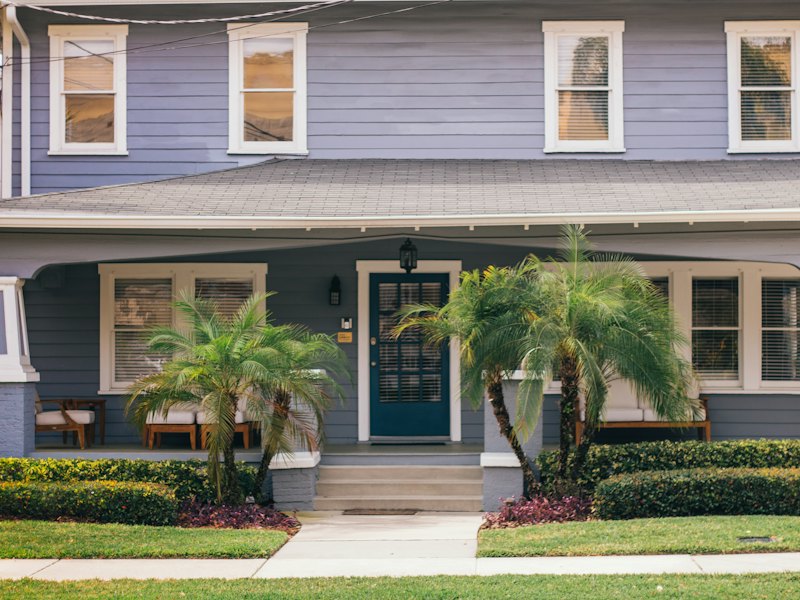 A blue two-story house with a front porch and palm trees