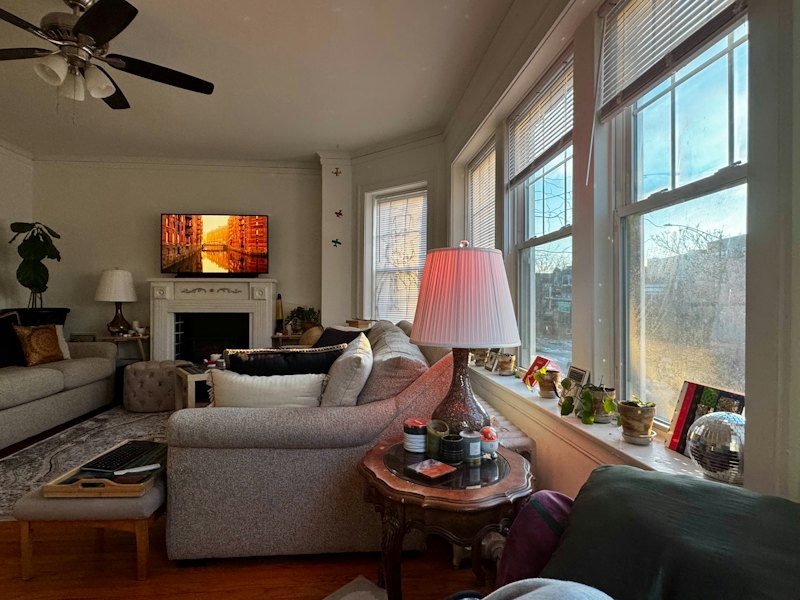 A cozy living room with a sofa, a lamp and big sunny windows